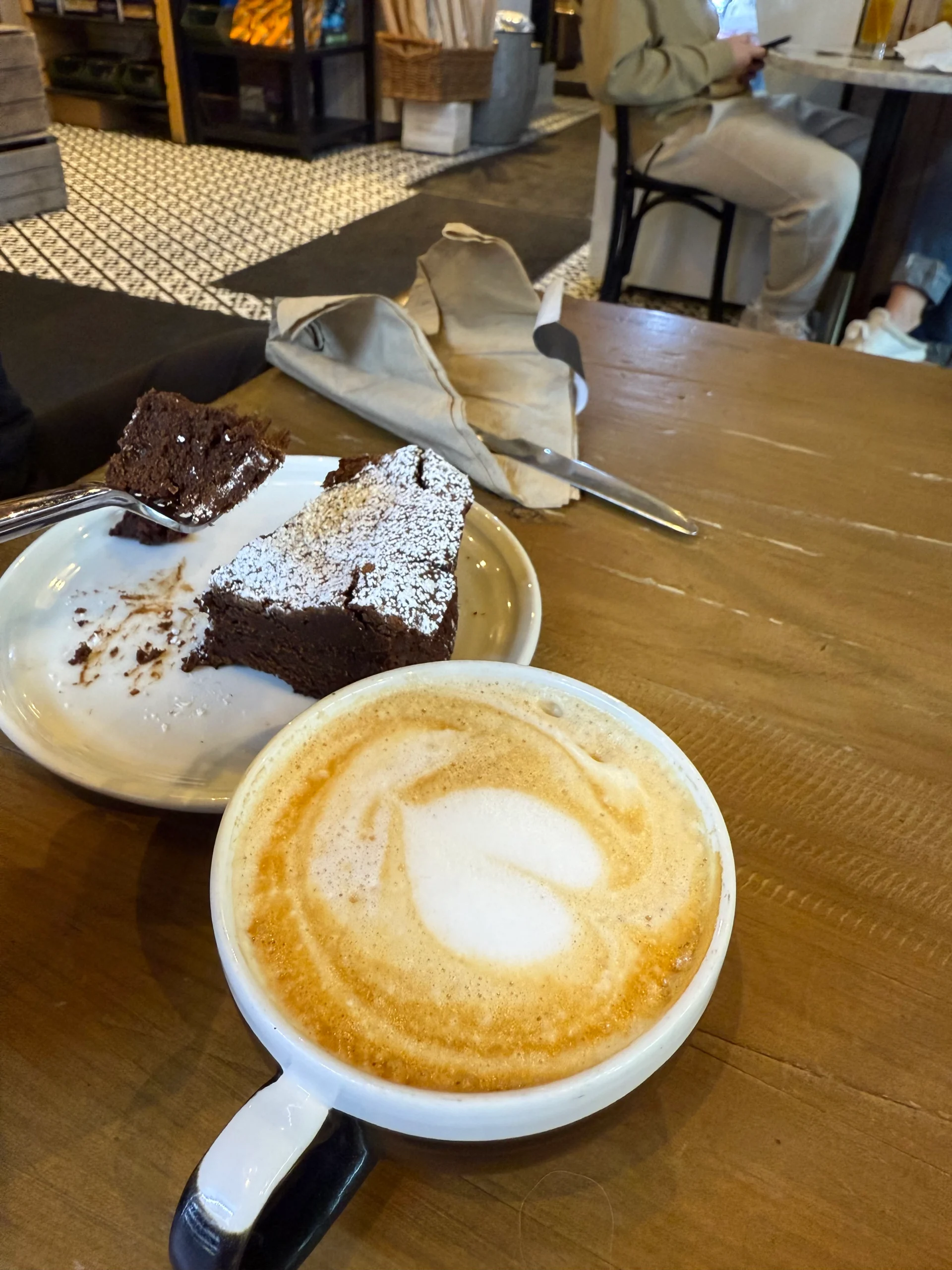 Partially eaten flourless chocolate cake with a cappuccino at Mediterra Cafe, showcasing a rich dessert experience.